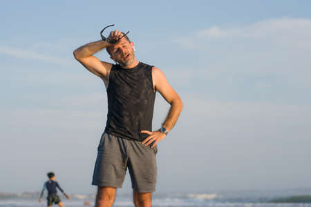 jogging Summer workout - young attractive and fit runner man training on beautiful beach breathing...