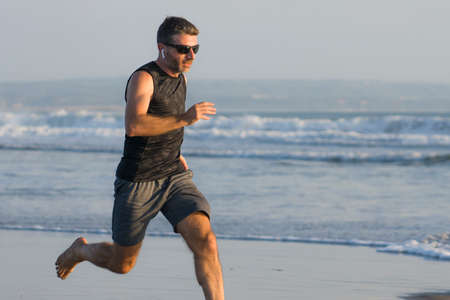 jogging Summer workout - young attractive and fit runner man training on beautiful beach running...