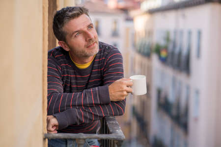 30s or 40s attractive and happy man at home balcony relaxed and cheerful enjoying cup of coffee...