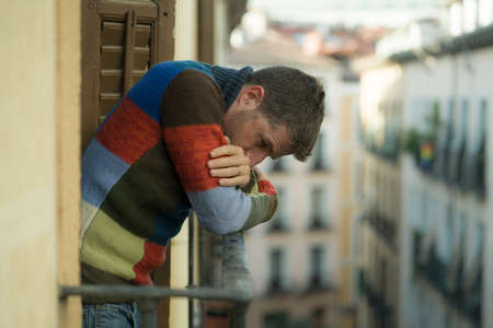 urban lifestyle emotional portrait of young attractive and depressed man at home balcony leaning...