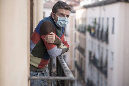 stay home quarantine portrait of of 30s handsome man in face mask sad and depressed at home balcony...