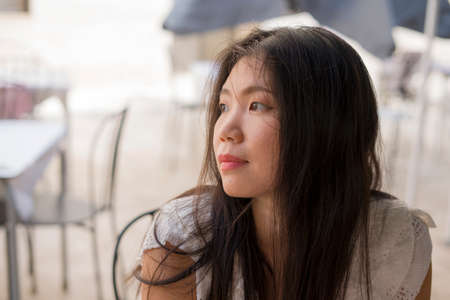 lifestyle portrait of young beautiful and sweet Asian Korean woman sitting outdoors at street cafe thoughtful and relaxedの写真素材