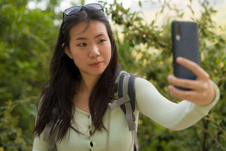 lifestyle portrait of young happy and beautiful Asian Japanese tourist woman visiting Europe during Summer holidays trip taking selfie with mobile phone enjoying old town landscapeの写真素材