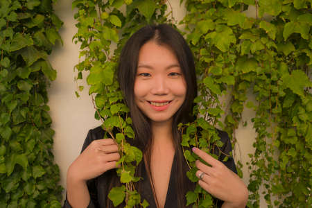 lifestyle portrait of young happy and beautiful Asian Chinese woman enjoying outdoors posing at village garden playful and cheerful in beauty fashion and freedom conceptの写真素材
