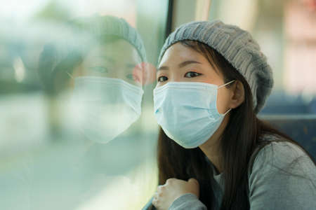 lifestyle portrait of young attractive and pretty Asian woman wearing mask in railcar traveling in...