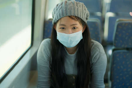 lifestyle portrait of young attractive and pretty Asian woman wearing mask in railcar traveling in new normal virus time - sweet Korean girl by train window smiling cheerfulの写真素材