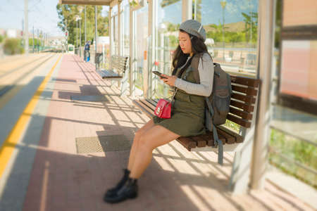 lifestyle portrait of young attractive and relaxed Asian Japanese woman sitting on bench at train...