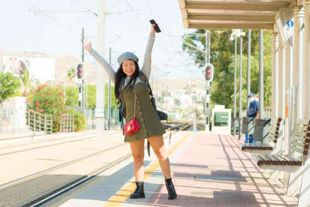 lifestyle portrait of young attractive and relaxed Asian Japanese woman sitting on bench at train...