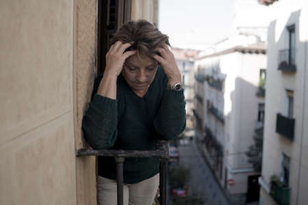 dramatic lifestyle portrait of mature woman on her 70s crying depressed and sad at home balcony...