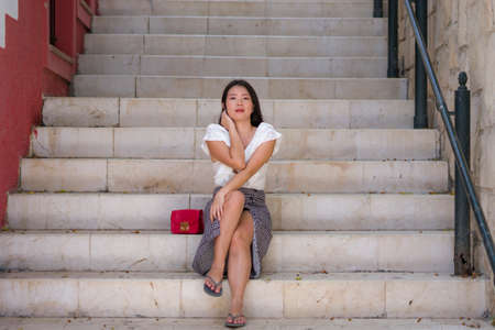 outdoors lifestyle portrait of young beautiful and happy Asian woman sitting on staircase - attractive Korean girl walking around Andalusia town in Spain enjoying tourist city tourの写真素材