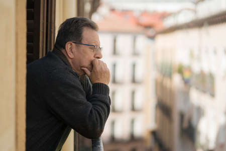 lifestyle portrait of sad and depressed mature man 65 to 70 years old at home balcony feeling lonely and confused facing getting old and retirement alone looking away thoughtful and lostの写真素材