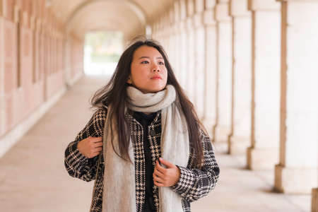 lifestyle portrait of young and beautiful Asian Korean tourist woman smiling happy enjoying city tour walking around historic district on a sunny winter day in holidays travel and tourismの写真素材