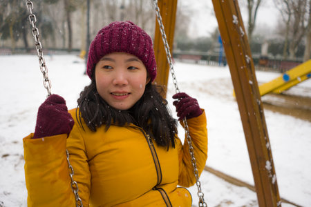young happy and attractive Asian Japanese woman in Winter jacket and beanie enjoying snowfall at...