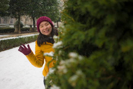 young happy and attractive Asian Japanese woman in Winter jacket and beanie enjoying snowfall at...