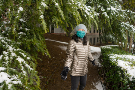 lifestyle portrait of  young happy and attractive Asian Chinese woman in winter hat and mask at beautiful city park playing with snow cheerful enjoying cold Christmas holidaysの写真素材