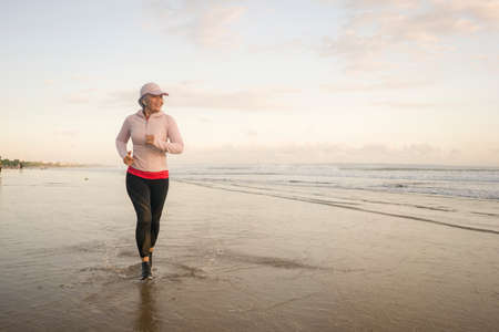 fit and attractive mature woman with grey hair doing beach workout on her 50s running on the beach happy and free in senior fitness selfcare and wellness conceptの写真素材