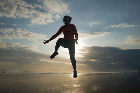 silhouette of happy and excited woman jumping on the air above sea water at beautiful beach on sunset in freedom and excitement conceptの写真素材