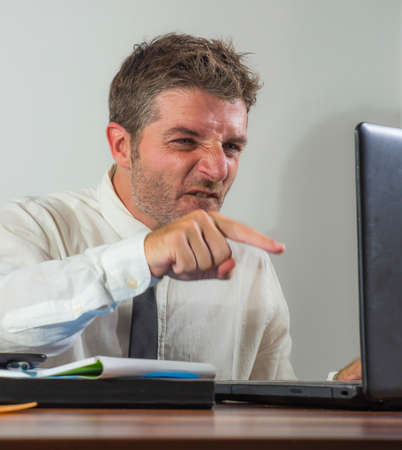 upset and angry businessman at computer desk in office- unhappy man working frustrated suffering stress as employee of corporate business complaining in rageの写真素材