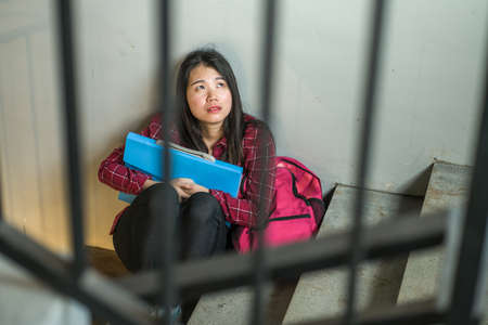 young depressed and scared Asian Japanese student girl suffering abuse and harassment at school victim of bullying and discrimination sitting on college staircase tormentedの写真素材