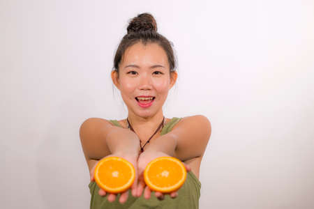 wellness and self care - young happy and beautiful Asian Japanese woman holding orange fruit sliced in half smiling cheerful in healthy nutrition and diet conceptの写真素材