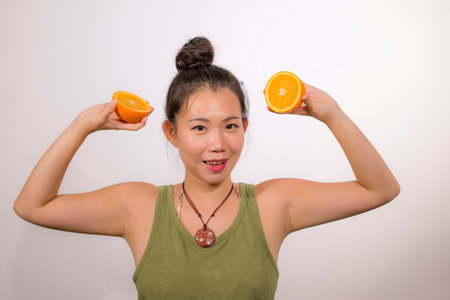 wellness and self care - young happy and beautiful Asian Chinese woman holding orange fruit sliced in half smiling cheerful in healthy nutrition and diet conceptの写真素材