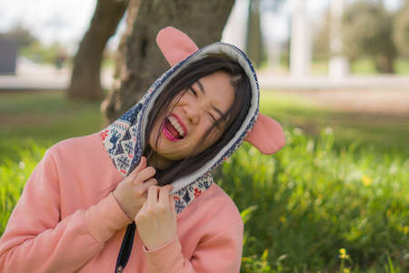 sweet Asian woman in hoodie making faces - lifestyle portrait of young happy and beautiful Japanese...