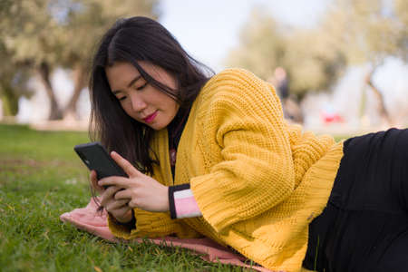relaxed Asian woman using mobile phone in city park - lifestyle portrait of young happy and pretty...