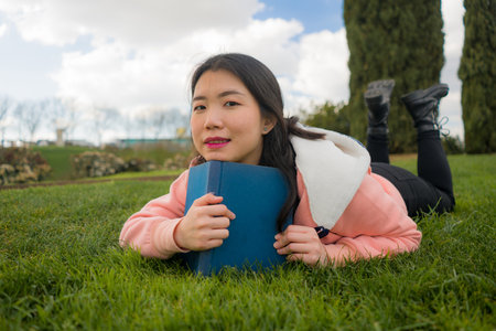 young Asian woman enjoying novel on grass - lifestyle portrait of young happy and pretty Japanese...