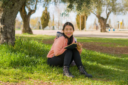 young Asian woman enjoying novel on grass - lifestyle portrait of young happy and pretty Japanese...