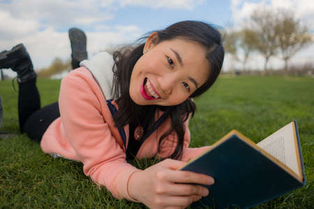 young Asian woman enjoying novel on grass - lifestyle portrait of young happy and pretty Japanese...