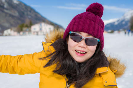 Winter holidays in the snow - lifestyle portrait of young happy and beautiful Asian Chinese girl...