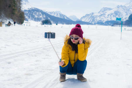 Winter holidays selfie in the snow - young happy and cheerful Asian Korean woman on taking self portrait with mobile phone in cold snowy mountain at Swiss Alpsの写真素材