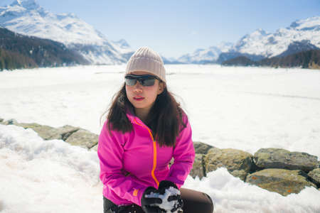 young Chinese woman enjoying amazing snowy landscape view - happy and beautiful Asian girl playing with snow in front of frozen lake and mountains during Swiss Alps holidayの写真素材