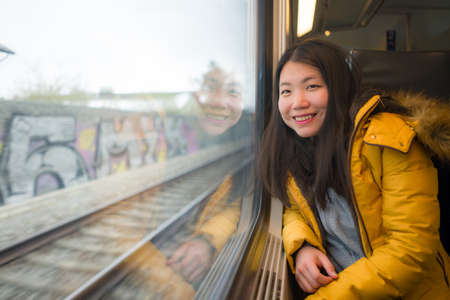 young beautiful and happy Asian Korean woman sitting on train looking out to window enjoying...