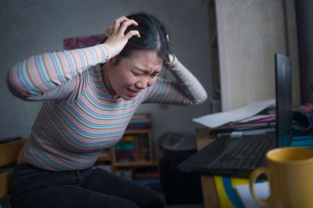 lifestyle portrait of young stressed and worried Asian Chinese woman working from home or studying...