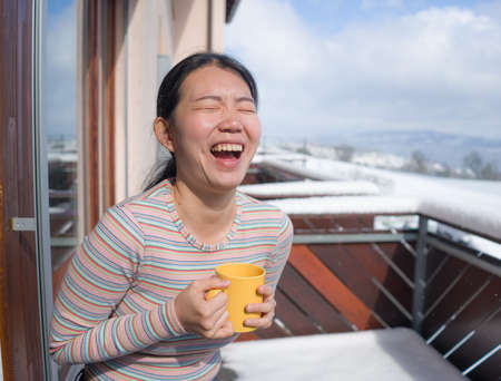 winter morning coffee - young happy and attractive Asian Japanese woman at hotel or home balcony in...