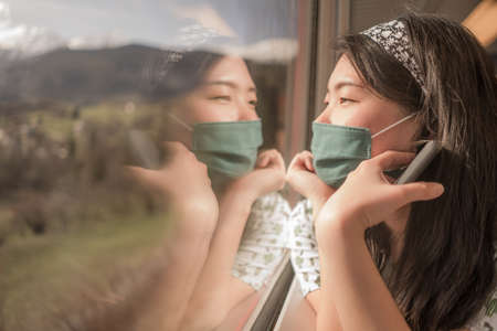 train travel in times- young happy and cute Asian Chinese woman in  face mask traveling on rail car...
