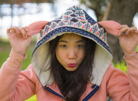 lifestyle portrait of young happy and beautiful Asian Chinese woman in pink hoodie enjoying cheerful at city green park next to tree in Spring weekend walkの写真素材