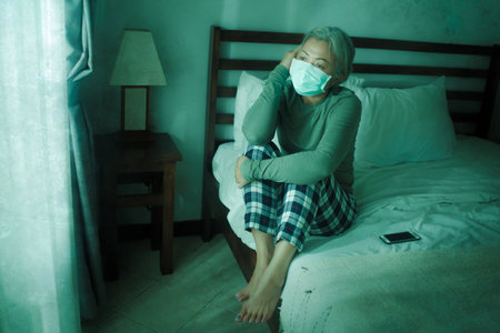 home dramatic portrait of  attractive middle aged woman 50s with grey hair and protective mask...