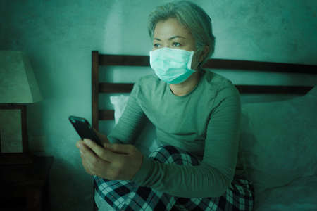 home dramatic portrait of  attractive middle aged woman 50s with grey hair and protective mask...