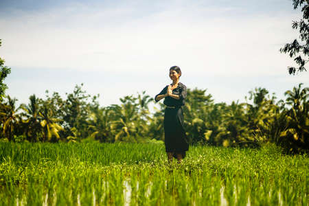 artistic portrait of young attractive and happy Asian woman outdoors at green rice field landscape dancing and doing spiritual meditation on beautiful nature backgroundの写真素材