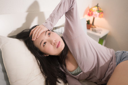 young Asian woman depressed - young beautiful and sad  Korean girl on bed with pillow feeling unhappy and broken heart suffering depression problem at home bedroomの写真素材