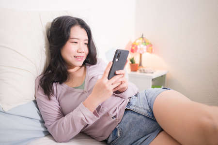 Asian girl with hand phone - home lifestyle portrait of young happy and attractive Korean woman on...