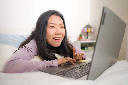 home lifestyle portrait of young Asian woman networking on bed -  beautiful and happy Japanese girl...