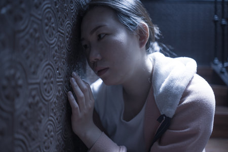 young beautiful Asian woman in pain suffering depression - dramatic indoors portrait on staircase of sad and depressed Chinese girl as victim of bullying and abuseの写真素材