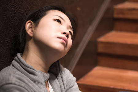 young beautiful Asian woman in pain suffering depression - dramatic indoors portrait on staircase of...