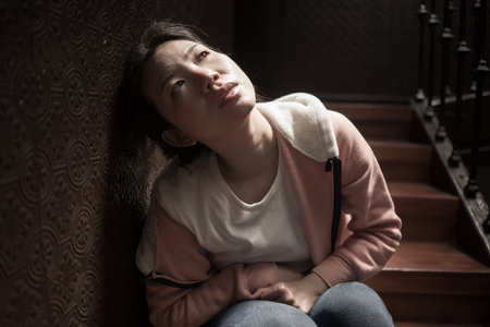 young beautiful Asian woman in pain suffering depression - dramatic indoors portrait on staircase of sad and depressed Chinese girl as victim of bullying and abuseの写真素材