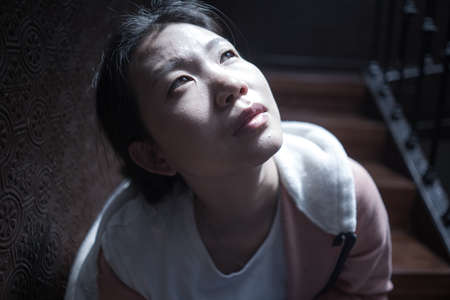 young beautiful Asian woman in pain suffering depression - dramatic indoors portrait on staircase of...