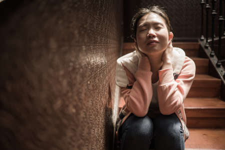 young beautiful Asian woman in pain suffering depression - dramatic indoors portrait on staircase of sad and depressed Korean girl as victim of bullying and abuseの写真素材