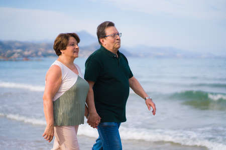 lifestyle portrait of loving happy and sweet mature couple - Latin senior retired husband and wife on 70s enjoying beach walk relaxed and cheerful celebrating love togetherの写真素材
